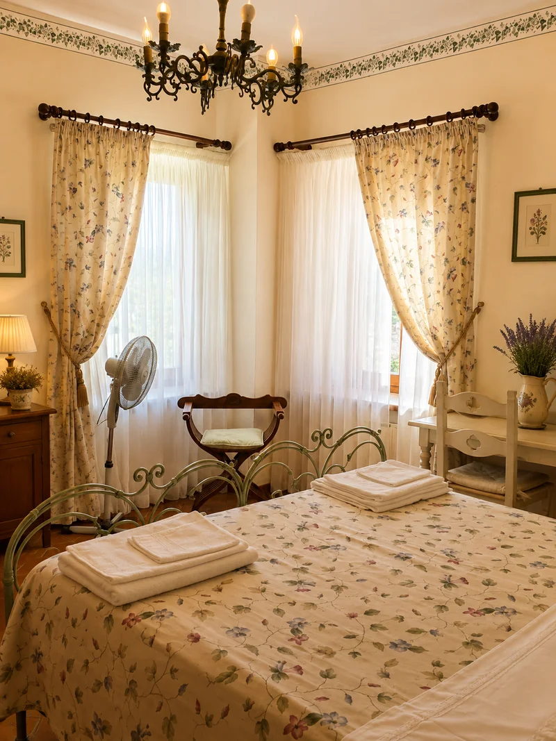 Camera con letto in ferro e tessuti a fiori, illuminata da due finestre