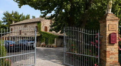 Il cancello d’ingresso in ferro battuto e la villa in pietra, con la targa La Rupe